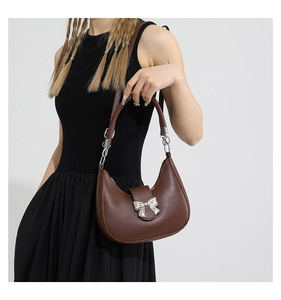 Gros plan d'un sac demi-lune marron avec nœud argenté porté sur une robe noire
