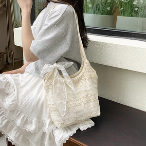 Elegant cream lace tote bag with floral patterns and a large bow in a summer setting