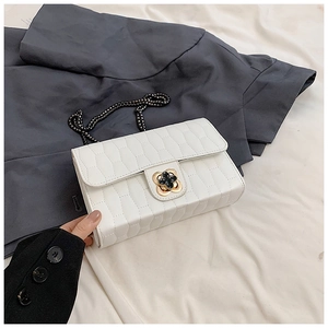 Detail of white quilted chain bag featuring a gold floral clasp with black crystal center