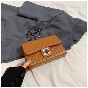 Detail of caramel brown quilted bag featuring a black floral clasp and leather chain strap