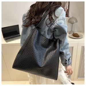 Détail d'un grand sac cabas en cuir tressé noir porté par un mannequin au quotidien