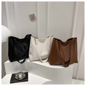 Trois grands sacs cabas à texture tissée en noir, blanc et marron sur un présentoir épuré