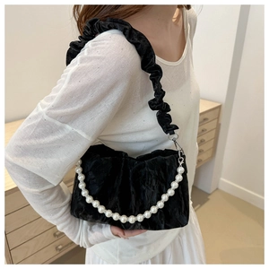 Close-up of black pleated shoulder bag with pearl chain and ruffled strap on model