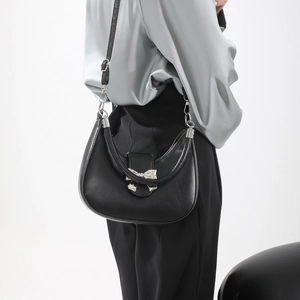Sac bandoulière demi-lune noir avec nœud argenté porté par un mannequin de mode