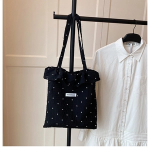 Détail du sac cabas noir à fleurs avec bords à volants et étiquette sur tissu froissé