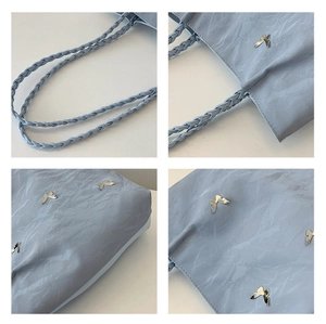 Detail of light blue tote bag featuring silver butterfly charms and woven shoulder straps