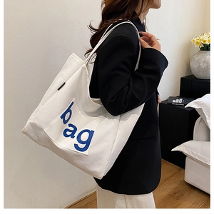 Detail of white canvas tote bag with blue bag letter print on model's shoulder