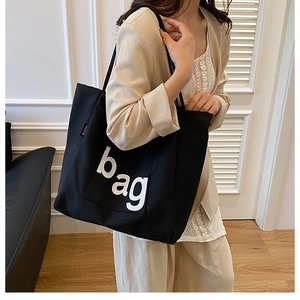 Fashionable black canvas tote bag with bold white lettering shown on model shoulder