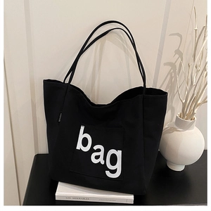 Détail d'un sac cabas noir en toile avec texte blanc posé sur des livres minimalistes