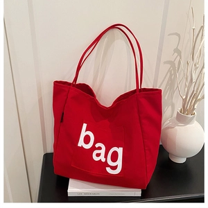 Detail of red canvas tote bag featuring front pocket and white letter print bag decoration