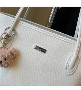 Detail of white woven leather tote bag featuring a metal logo and a cute brown plush bear charm