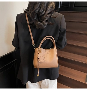 Detail of a brown lychee pattern leather bucket bag with a dog charm and shoulder strap