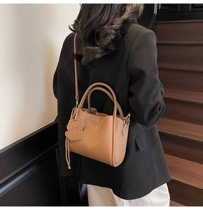 Close-up of caramel pebbled leather handbag featuring dog charm and brand embossing