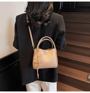 Detail view of beige leather bucket bag with litchi texture and cute bear pendant