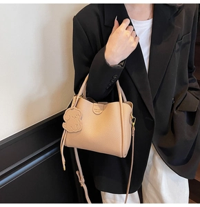 Detail of beige lychee leather bucket bag with puppy charm and brand embossing