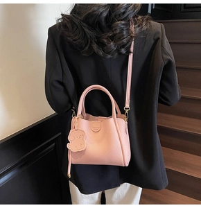 Pink lychee texture bucket bag with puppy charm shown against a black blazer background