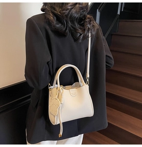 Detail of cream-colored pebble leather bucket bag featuring dog charm on wooden steps