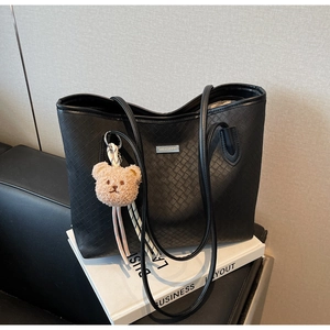 Close-up of black woven tote bag featuring silver logo and brown teddy bear charm