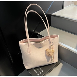 Detail of pink woven tote bag with a cute bear charm and metallic logo on books