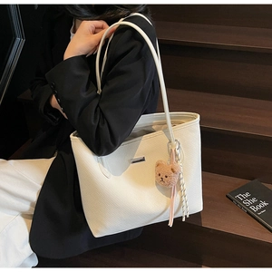 Detail of off-white woven tote bag with metal logo, bear charm and long shoulder strap