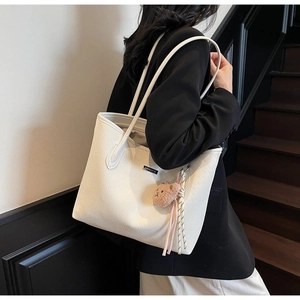 Detail of white woven texture tote bag with brown plush bear charm and metallic logo