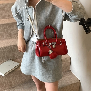 Red glossy Kelly style handbag with pearl chain strap and heart charm on a model