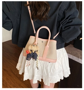 Detail of pink and beige canvas bucket bag with cute bear charm worn by a model