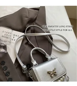 Détail du sac argenté avec fermoir papillon en métal et bandoulière en perles blanches