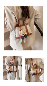 Three-way view of a beige canvas bucket bag with brown leather handles and a plush bear charm