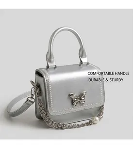 Détail du sac à main en cuir argenté avec boucle papillon et bandoulière en perles