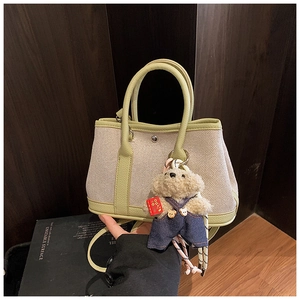 Detail of canvas bucket bag with green leather trim and a cute teddy bear charm