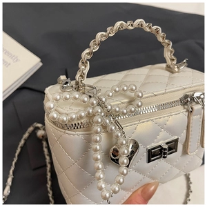 Detail van witte gewatteerde box-tas met gedraaid metalen handvat en parelmoer hartbedel