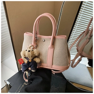 Detail of beige canvas bucket bag with pink leather trim and teddy bear charm accessory