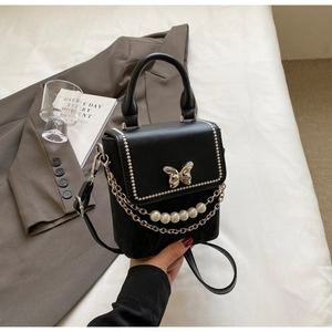 Détail d'un sac noir bandoulière avec boucle papillon argentée et chaîne de perles chic