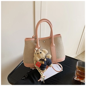 Close-up of canvas bucket bag with pink leather trim and a cute teddy bear charm