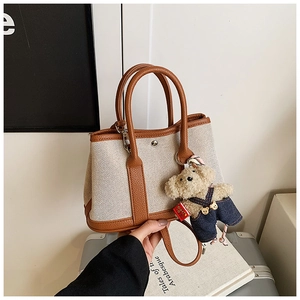 Detail of canvas bucket bag with brown leather trim and a cute teddy bear charm