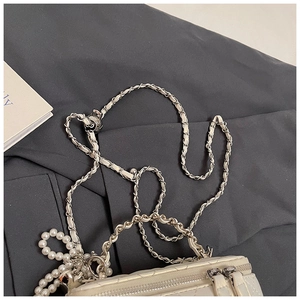 Macro detail van de gewatteerde crème tas met leren ketting en elegante parelhangers