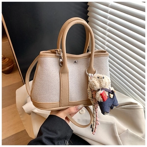 Detail of canvas bucket bag with leather handles, shoulder strap and a plush bear charm
