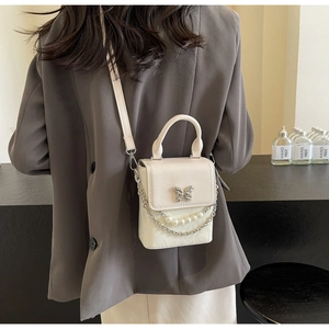 Détail du sac bandoulière avec boucle papillon argentée et élégante chaîne de perles