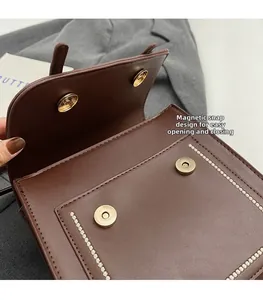 Detalle de bolso de cuero marrón con cierre magnético y costuras blancas en contraste