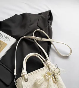 Detail of white lychee texture bucket bag with pearl bow charm on a grey suit jacket