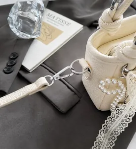 Detail of cream bucket bag with silver hardware, pearl charm and lace decor