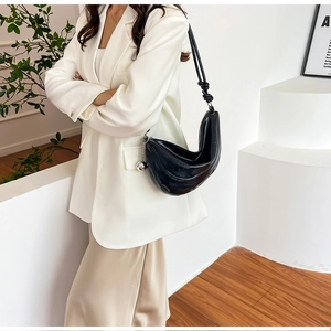 Detail of black glossy crescent bag with knot strap and silver metallic charm