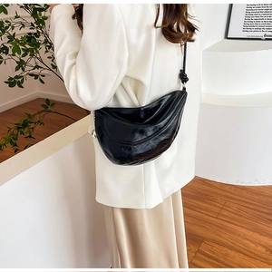 Detail of black glossy crescent shoulder bag showing textured faux leather and knotted strap