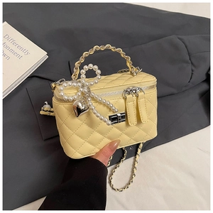 Detail van gele gewatteerde box-tas met zilveren sluiting en parelmoer strik hanger