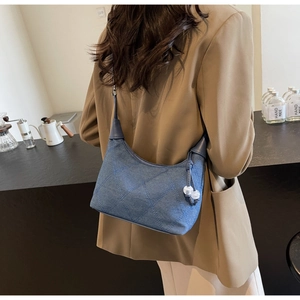Détail d'un sac d'épaule en denim bleu avec matelassage en losange et breloques perlées