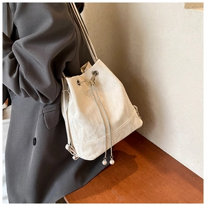 Detail view of cream bucket bag with drawstring closure and elegant pearl pendant