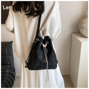 Detail of black pleated bucket bag featuring silver butterfly and pearl drawstring tassels