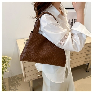 Bolso tote trenzado marrón oscuro sostenido por modelo en un interior cálido