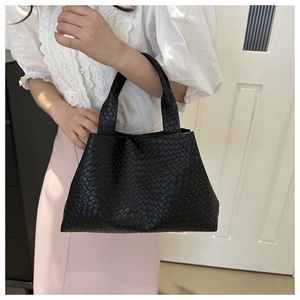 Close-up of black woven leather tote bag with thick texture held by a person